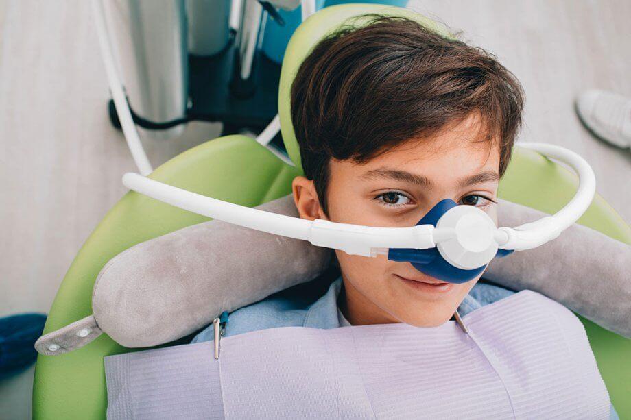 Boy with a nitrous oxide mask on smiling before his painless dentistry cleaning begins.